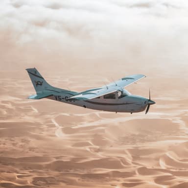 small airplane with retractable gear flying over dunes of sand